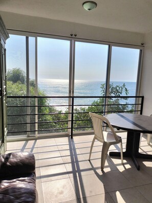 A balcony with a view of the sea, a table, and a chair.