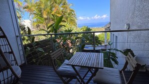 A covered outdoor area with a wooden table and chairs, a railing, and a view of palm trees and a building. - Villa Savane - Ocean view & Swimming pool, Reunion Island (Saint-Leu)