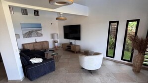A spacious living area with a sofa, a white armchair, a TV, and a ceiling fan. - Villa Savane - Ocean view & Swimming pool, Reunion Island (Saint-Leu)