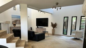 A spacious living area with a flat-screen TV, a staircase, and a large window. - Villa Savane - Ocean view & Swimming pool, Reunion Island (Saint-Leu)