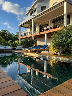 Un bâtiment à deux étages doté d’une piscine, de chaises longues et d’une terrasse en bois.