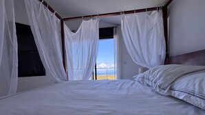 A bedroom with a large bed, white curtains, and a view of the outdoors. - Villa Savane - Ocean view & Swimming pool, Reunion Island (Saint-Leu)