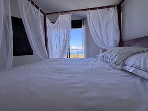 Ein Schlafzimmer mit einem großen Bett, weißen Vorhängen und Blick ins Freie.
