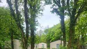 A grassy area with a white fence, a wooden deck, and a row of mobile homes. - Remarkable 3-bed Lodge in St Minver (Wadebridge)