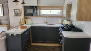 A compact kitchen with a microwave, stove, and sink, featuring dark cabinetry and a marble countertop. - Remarkable 3-bed Lodge in St Minver (Wadebridge)