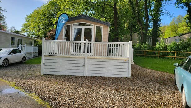 A small, single-story building with a white fence, a 'For Sale' sign, and a car parked nearby. - Remarkable 3-bed Lodge in St Minver (Wadebridge)