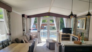A room with a wooden dining table, a sofa, a television, and a desk with drawers. - Remarkable 3-bed Lodge in St Minver (Wadebridge)
