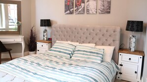 A bedroom with a tufted headboard, a striped bedspread, two bedside tables with lamps, and a wall-mounted artwork. - Stylish Comfort in the Heart of Sheffield (Sheffield)