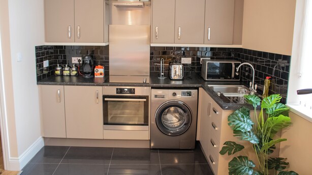 A modern kitchen with stainless steel appliances, a built-in oven, a washing machine, and a microwave. - Stylish Comfort in the Heart of Sheffield (Sheffield)