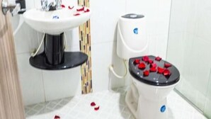 A bathroom with a round mirror, a white sink, a toilet with red heart-shaped decorations, and a patterned floor. - Hotel Veneton  (Dosquebradas)