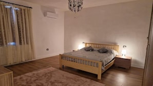 A bedroom with a wooden bed, bedside tables, a rug, and a chandelier. - Tuscan Villa Retreat in San Romano (Montopoli in Val d'Arno)