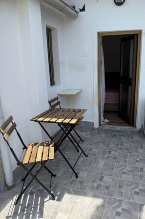 Une terrasse avec une table et des chaises en bois, une petite fenêtre et une porte donnant sur un espace intérieur.