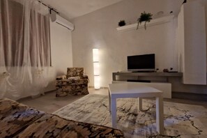 A living room with a flat-screen TV, a white table, a patterned armchair, a floor lamp, and a large window with curtains. - Tuscan Villa Retreat in San Romano (Montopoli in Val d'Arno)