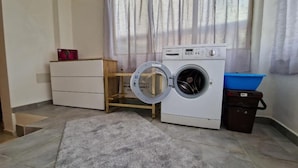 A laundry room with a front-loading washing machine, a wooden cabinet, a blue basin, and a grey rug. - Tuscan Villa Retreat in San Romano (Montopoli in Val d'Arno)
