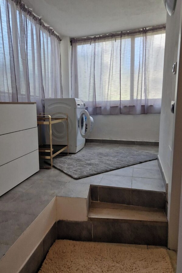A laundry area with a washing machine, a drying rack, and a small step leading to a door.