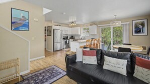 A modern kitchen with white cabinets, a stainless steel refrigerator, and a dining area with a round table and chairs. - Beach Please | Hot tub and Dog Friendly Sleeps 8 (Rockaway Beach)
