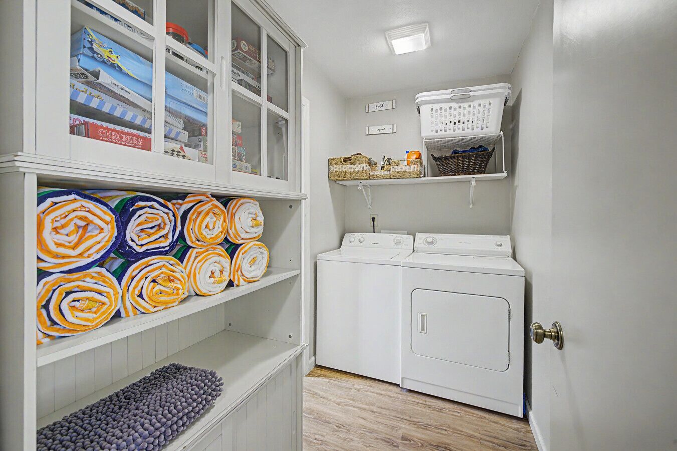 Een wasserette met een witte wasmachine, een plank met opgevouwen handdoeken en een mand aan de muur.