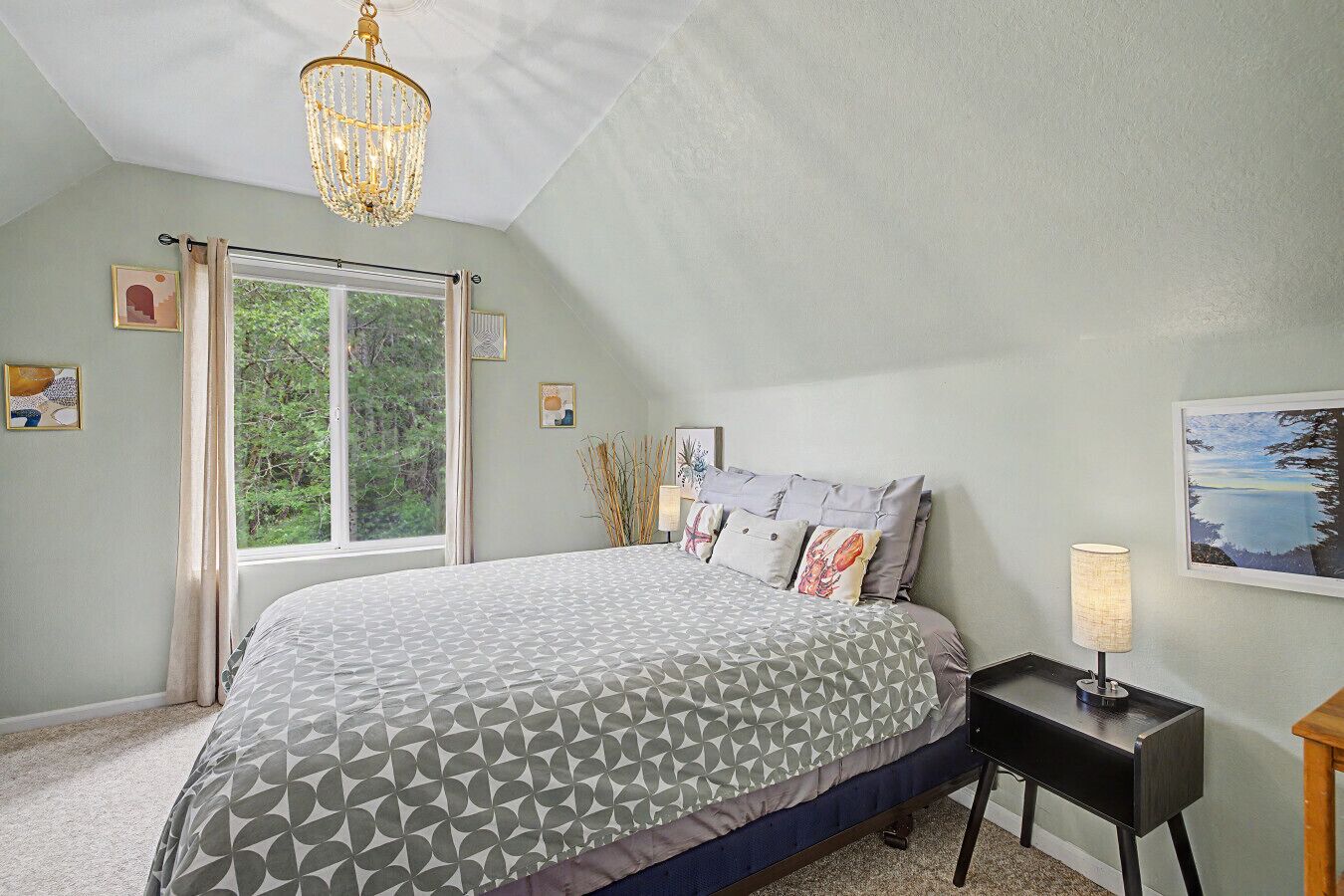 A bedroom with a bed, a chandelier, a bedside table with a lamp, and a window with curtains.
