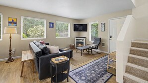 A living room with a sofa, a fireplace, a TV, and a staircase. - Beach Please | Hot tub and Dog Friendly Sleeps 8 (Rockaway Beach)