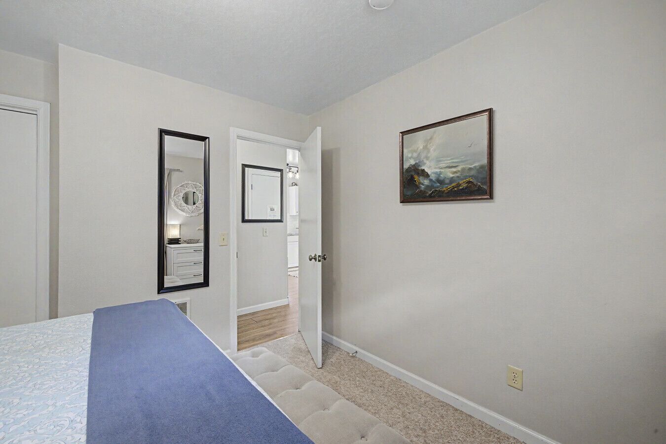 A bedroom with a bed, a door leading to a bathroom, and a painting on the wall.