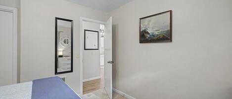A bedroom with a bed, a door leading to a bathroom, and a painting on the wall.