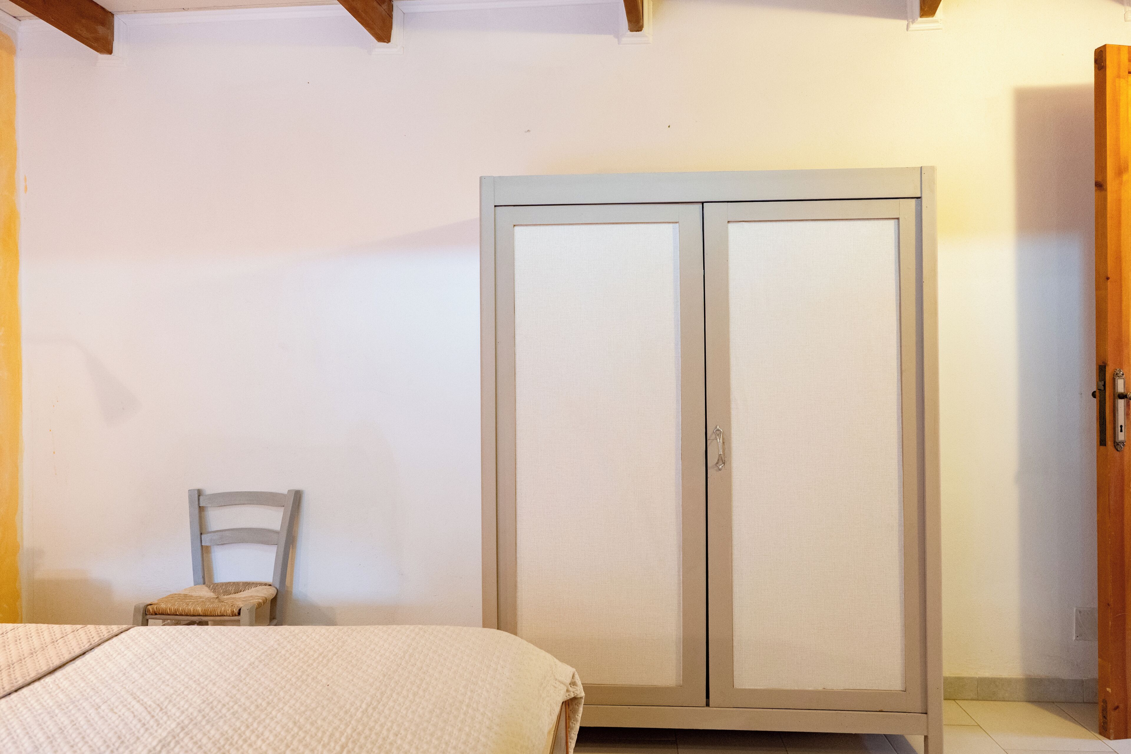 Un dormitorio con cama, armario y una silla.