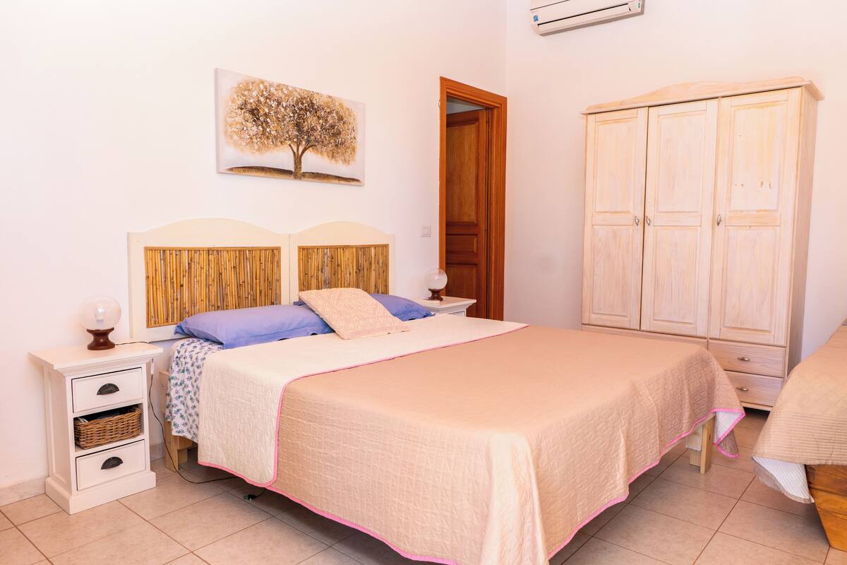 Quarto com cama, mesas de cabeceira, guarda-roupa e ar-condicionado fixado na parede.