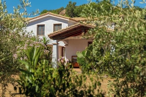 Una casa con fachada blanca, techo de madera y un jardín con diversas plantas.