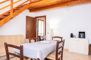 Un comedor con una mesa preparada para dos personas, sillas de madera, un armario blanco y una escalera de madera.