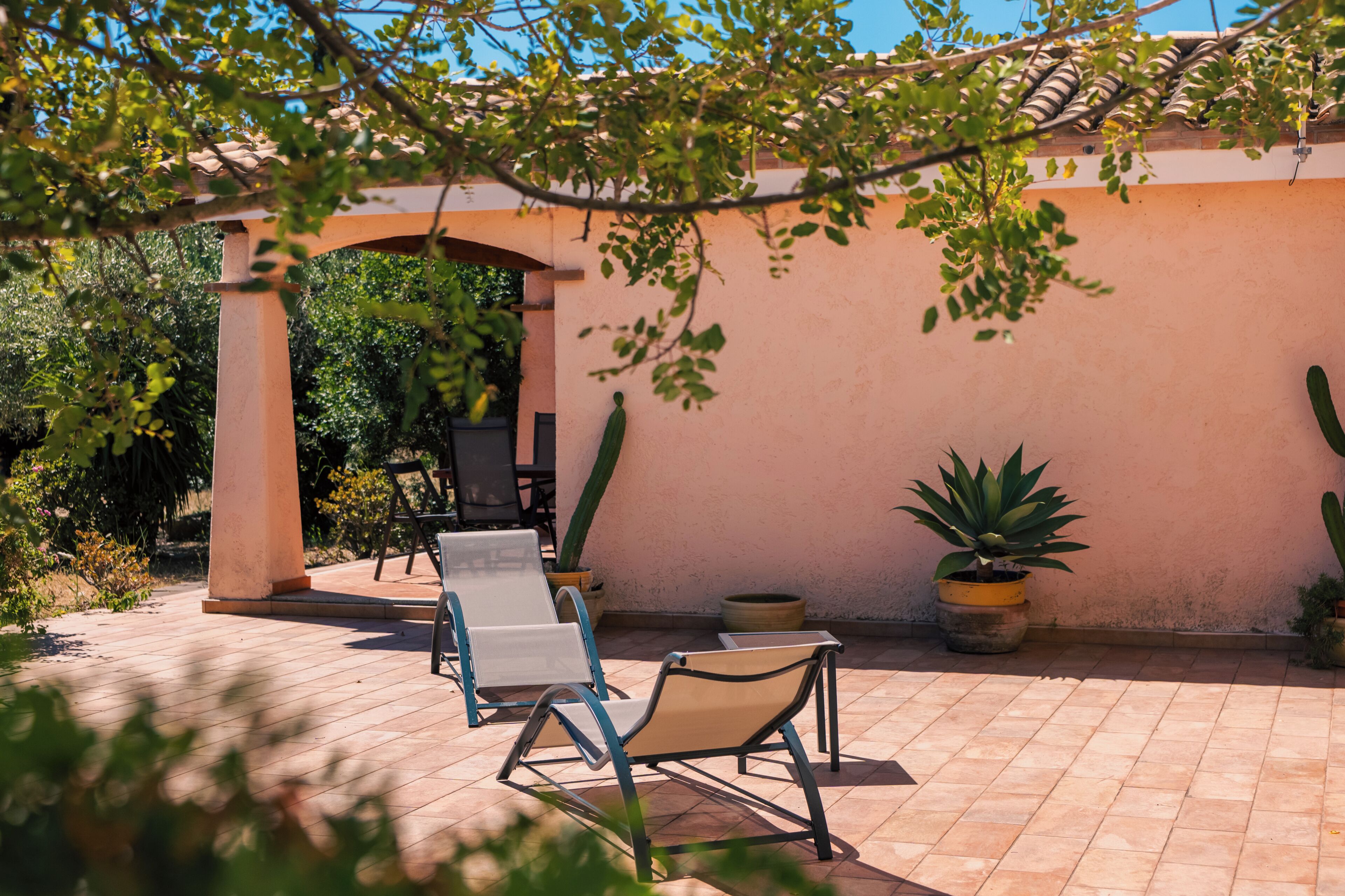 A patio with two lounge chairs, a pergola, and potted plants.