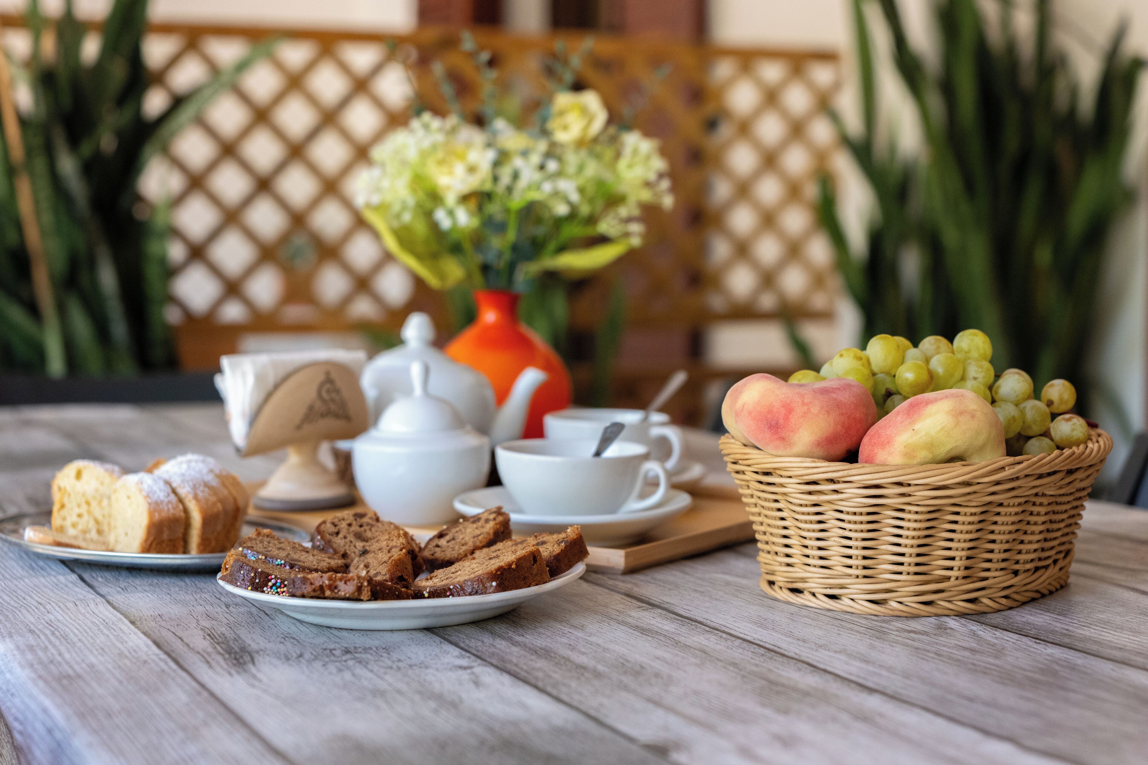 Une table avec une assiette de tranches de pain, un panier de fruits et une théière.