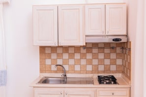 A kitchen with white cabinets, a tiled backsplash, a stainless steel sink, and a gas stove. - Residenze Camboni (Castiadas)