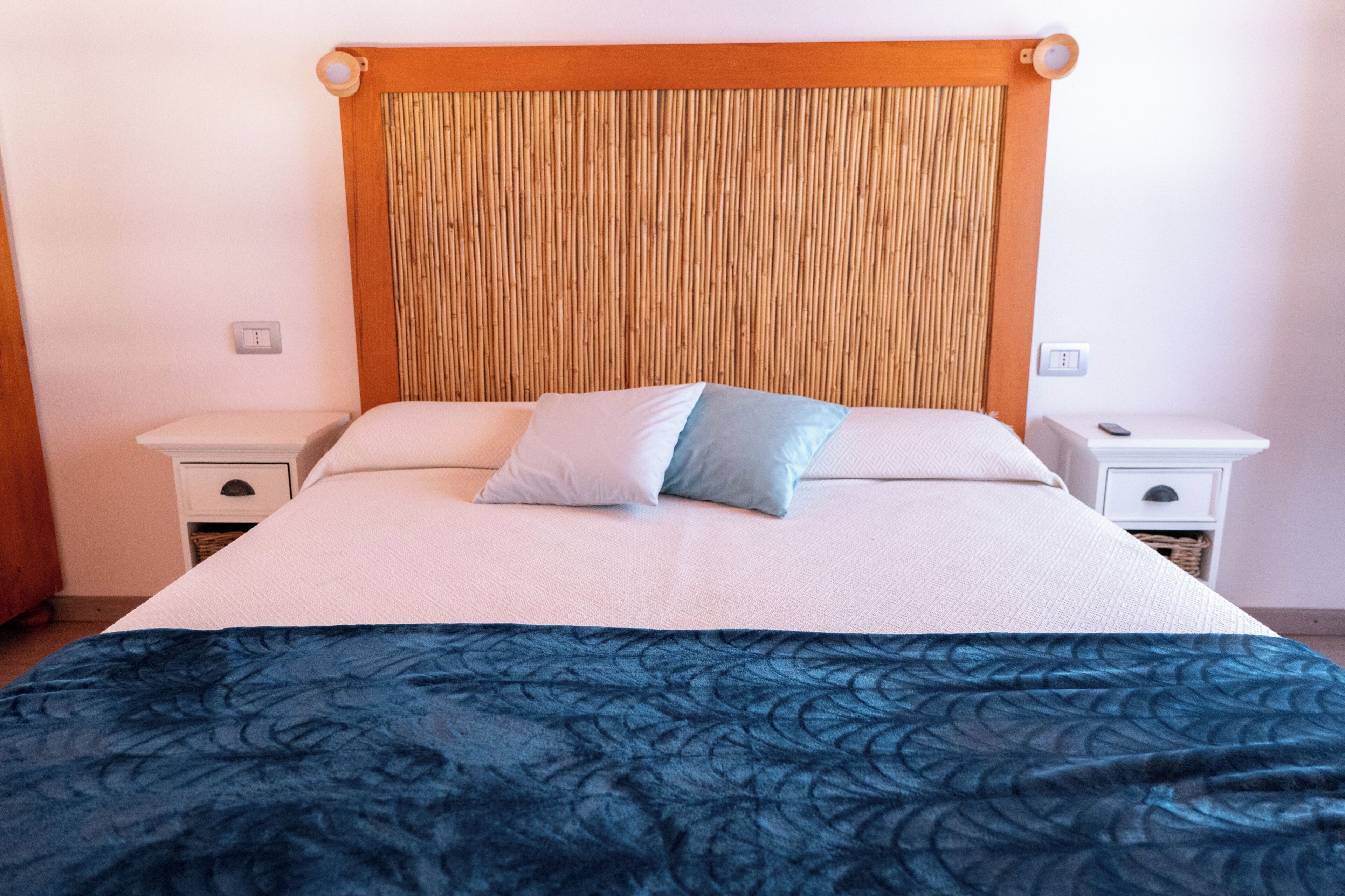 Una cama con cabecera de madera, dos mesitas de noche y un edredón azul estampado.