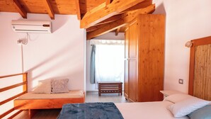Een slaapkamer met een bed, een bankje, een airconditioning, houten balken en een kledingkast.