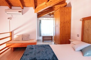 A bedroom with a bed, a bench, an air conditioning unit, wooden beams, and a wardrobe. - Residenze Camboni (Castiadas)
