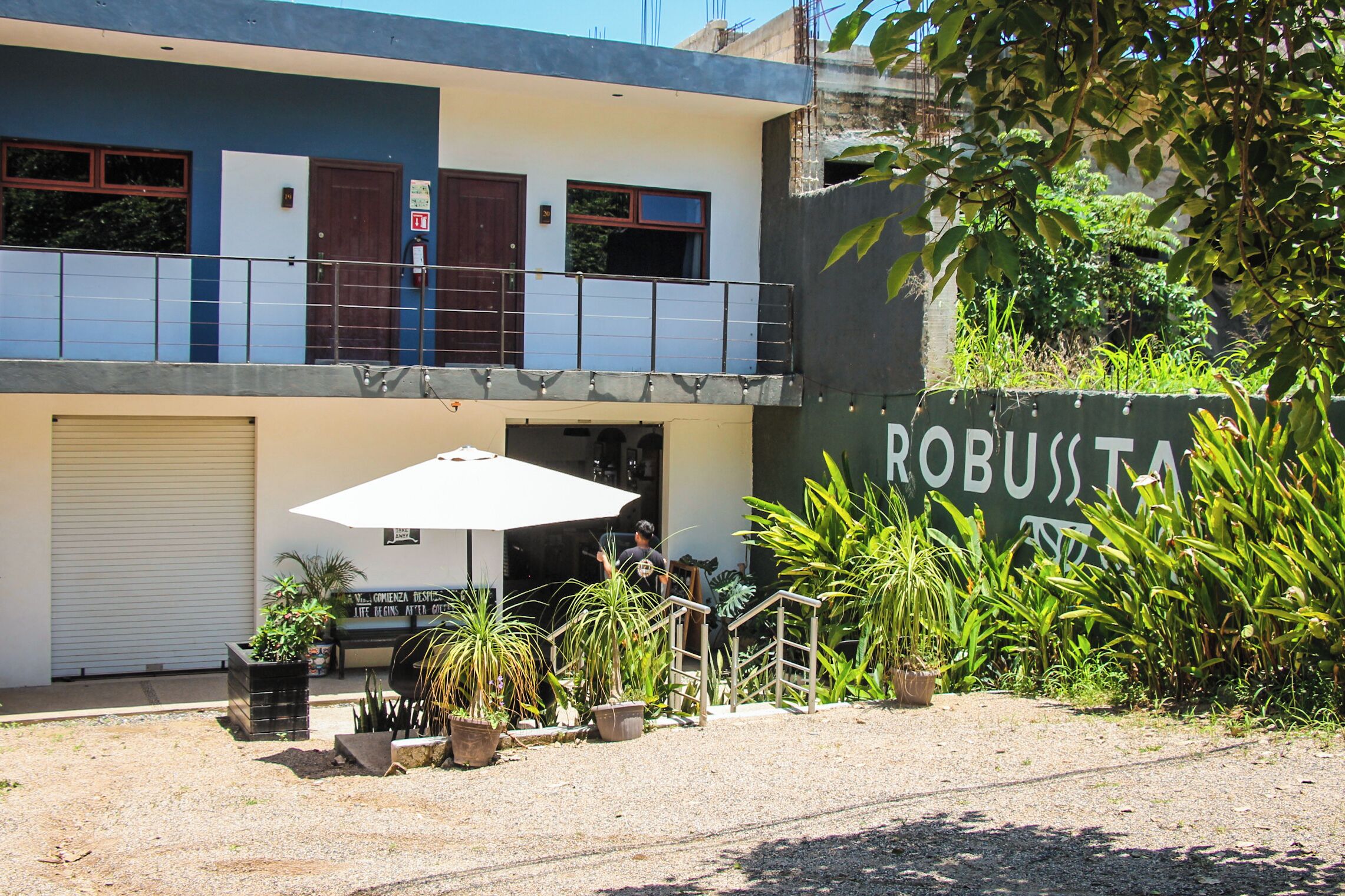 A two-story building with a balcony, potted plants, and a sign that reads 'ROBUSTA.'