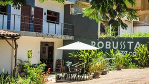 Un bâtiment sur lequel on peut lire l’inscription « ROBUSTA », avec une terrasse comprenant des tables et des chaises, ainsi que des plantes en pot.