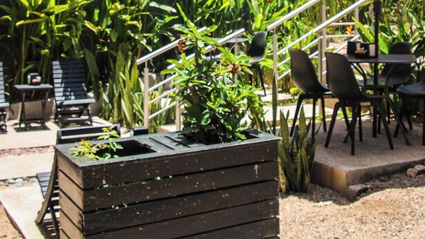 Un espace extérieur aménagé avec un bac à fleurs en bois, des chaises d’extérieur et une table placée sous un parasol.