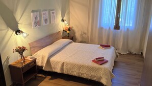A neatly made bed with a white blanket, a bedside table with a vase of flowers, and a wall-mounted light fixture. - Su Entu Suite Free Parking 5 min from the sea (Giba)