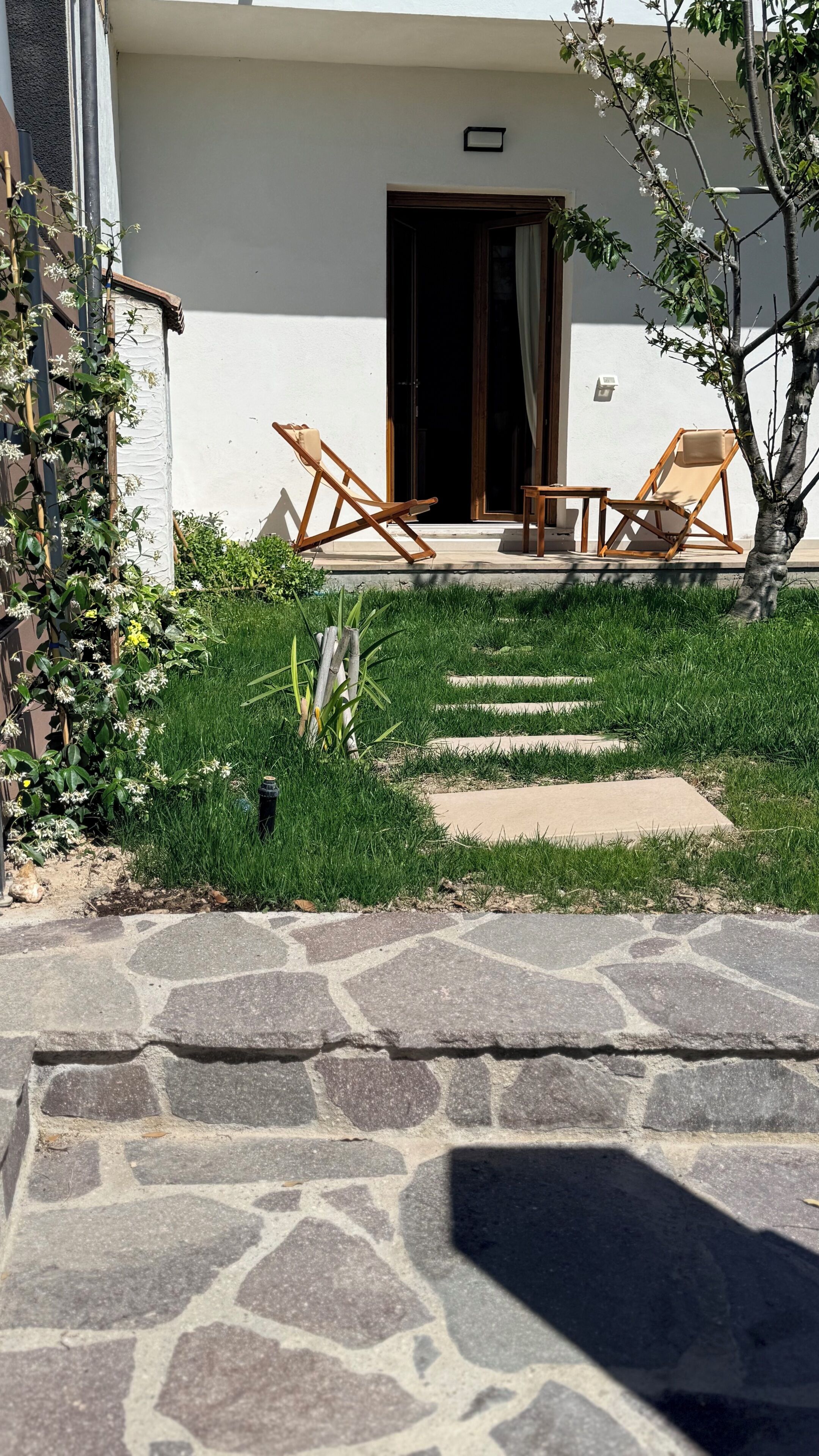 A stone pathway leading to a building with two wooden lounge chairs and a small table.