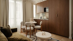 Ein modernes Wohnzimmer mit Sofa, Esstisch mit Stühlen und einer Küchenzeile mit Holzschränken und einer Mikrowelle.