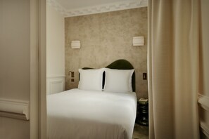 Quarto de hotel com uma cama grande, paredes bege e duas luminárias fixadas na parede.