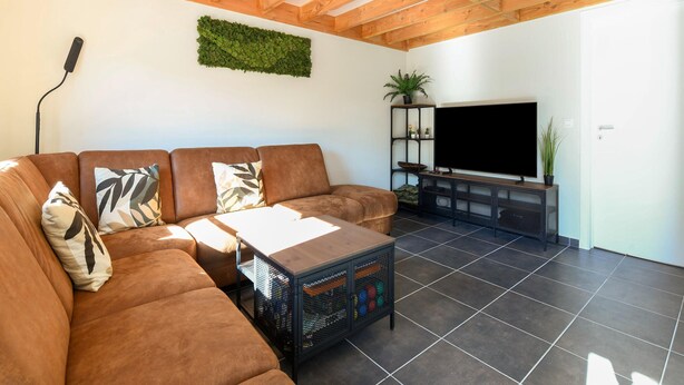 A living room with a sectional sofa, a coffee table, a TV on a stand, and a green wall decoration. - Holiday Home in Koksijde Near Sandy Beaches (Koksijde)
