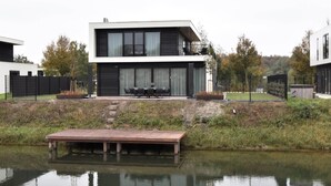 A modern two-story house with a flat roof, large windows, and a deck overlooking a body of water. - Luxury 10p Villa on the Water Near Harderwijk (Zeewolde)