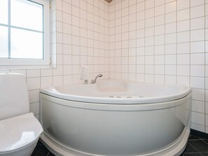 A bathroom with a white bathtub, a toilet, and a window. - 4 Star Holiday Home in Norre Nebel (Norre Nebel)