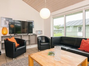 A modern living room with a TV, leather sofas, a wooden coffee table, and a large window with a view of a building. - 4 Star Holiday Home in Norre Nebel (Norre Nebel)