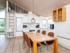A modern kitchen with a wooden dining table, chairs, and a built-in oven. - 4 Star Holiday Home in Norre Nebel (Norre Nebel)