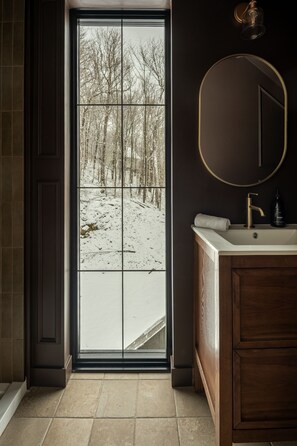 A bathroom with a large window, a round mirror, and a wooden vanity.