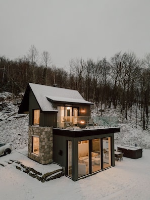 A modern house with a stone base, a balcony, and a glass-enclosed living area.