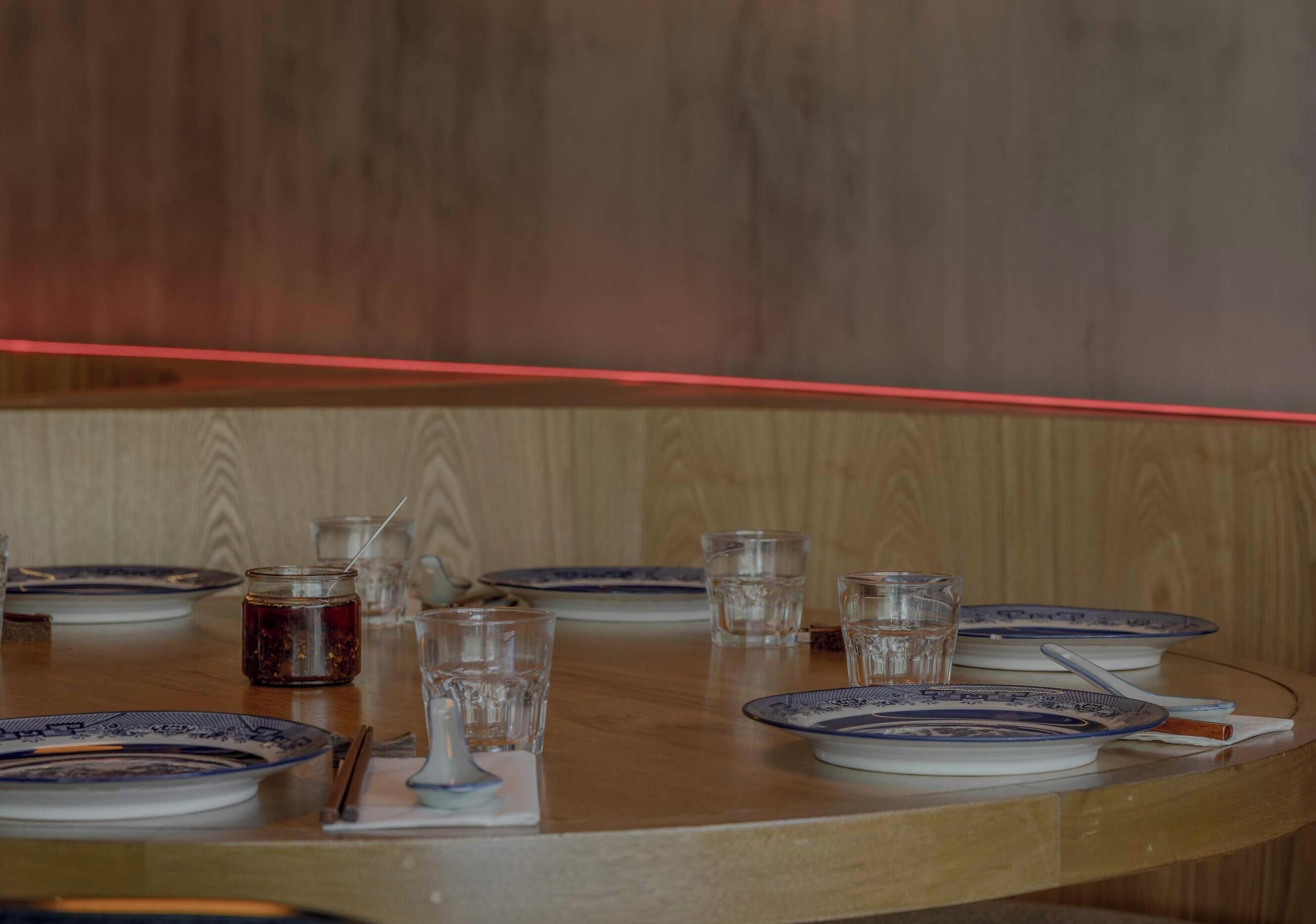 A round wooden table with plates, glasses, and a jar, set against a wooden wall.